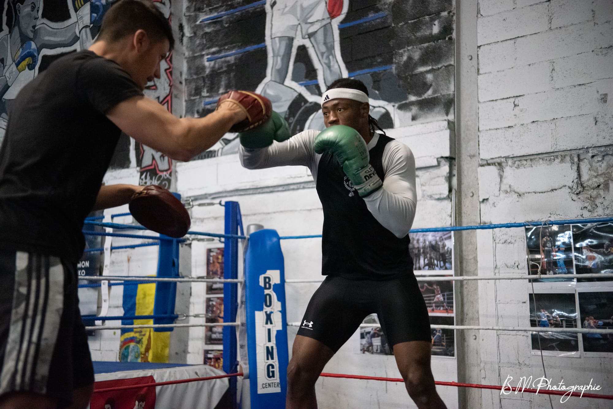 Un boxeur en garde travaille aux pattes d’ours face à son coach, dans le ring.
