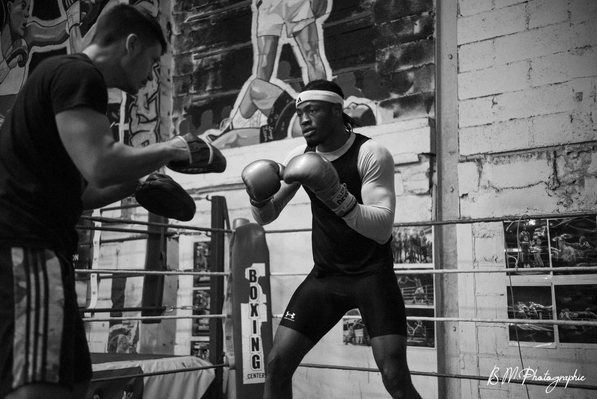 Un boxeur poings serrés en garde face à son coach, sous les projecteurs du ring.